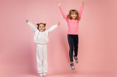 Astonished. Happy kids, girls isolated on coral pink studio background. Look happy, cheerful. Copyspace for ad. Childhood, education, emotions, facial expression concept. Jumping, running
